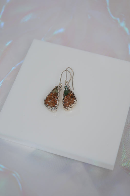 Teardrop-shaped earrings on a white card with a blurred background
