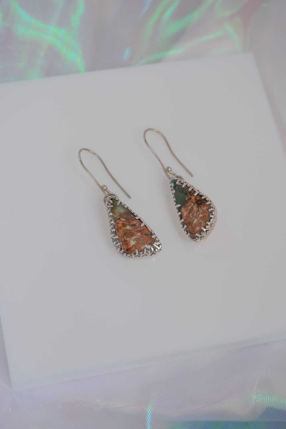 Teardrop-shaped earrings with orange and green stones on a white card.