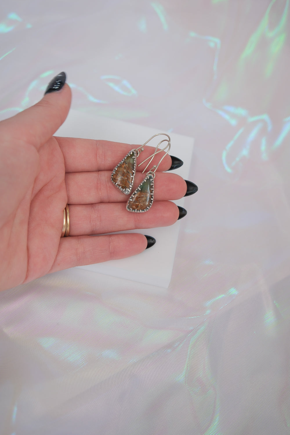 Hand holding a pair of teardrop-shaped earrings with a blurred background