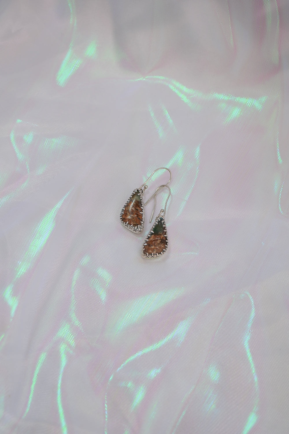 Teardrop-shaped earrings on a textured pink surface with green lighting.