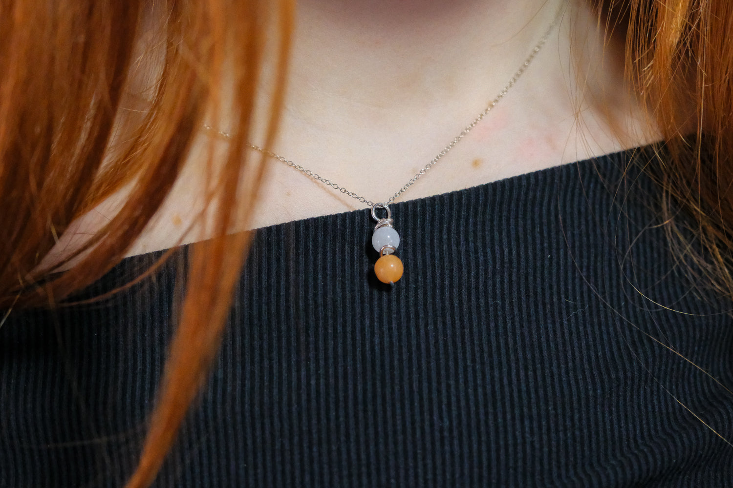 Necklace with three beads worn by a person with red hair.