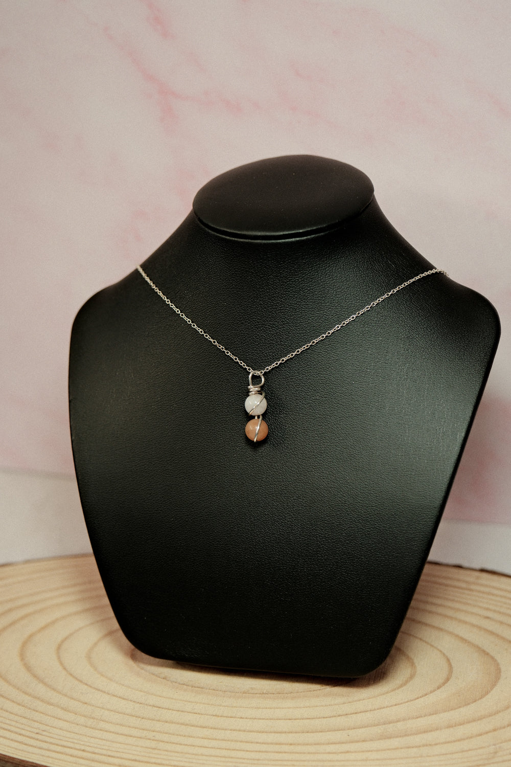 Necklace with a pendant on a black mannequin bust against a pink background