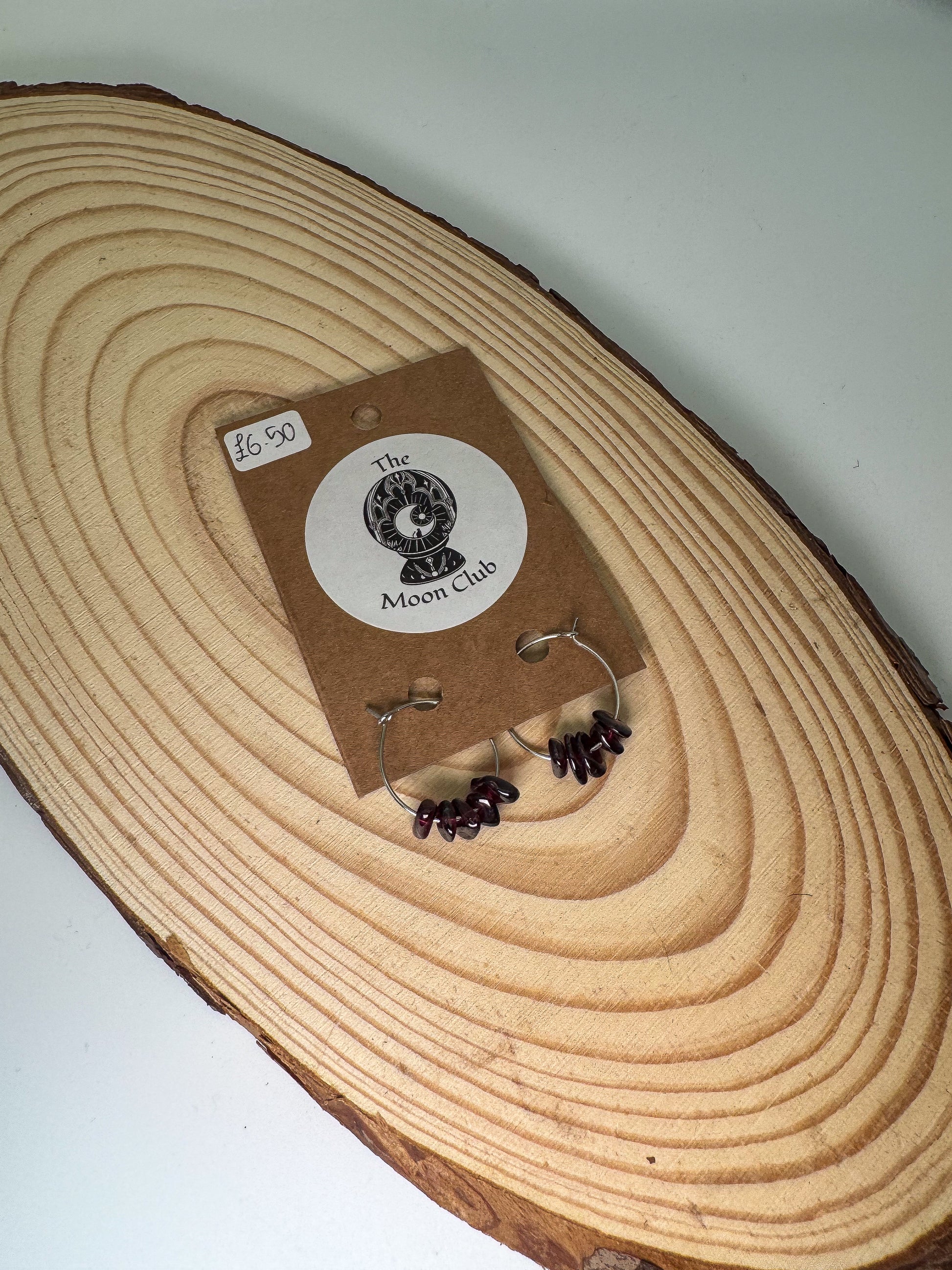 Garnet earrings on a wooden display with a 'The Moon Club' label.