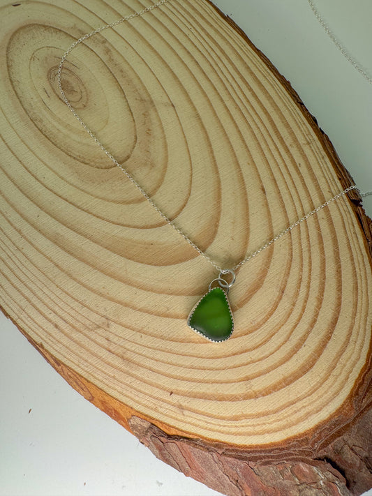 Green sea glass pendant on a chain on a wooden surface