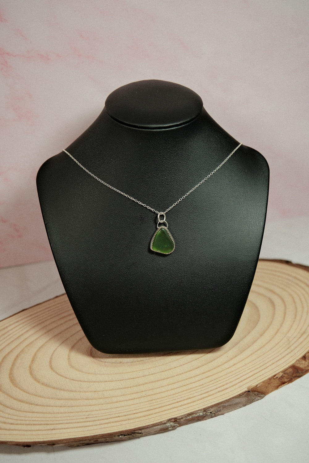 Green pendant necklace on a black mannequin bust with a pink and white background