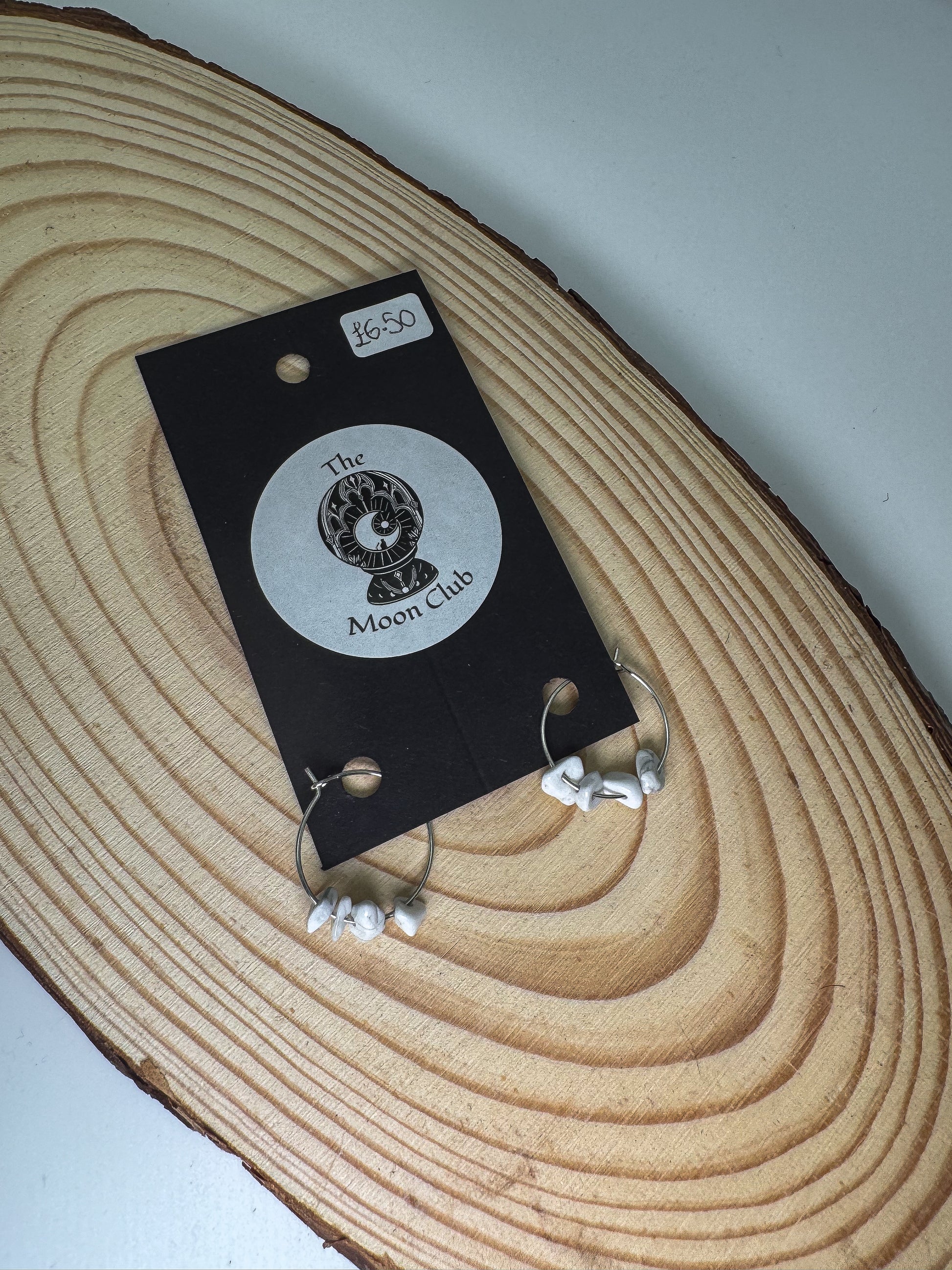 Howlite earrings on a black card with 'The Moon Club' logo on a wooden surface