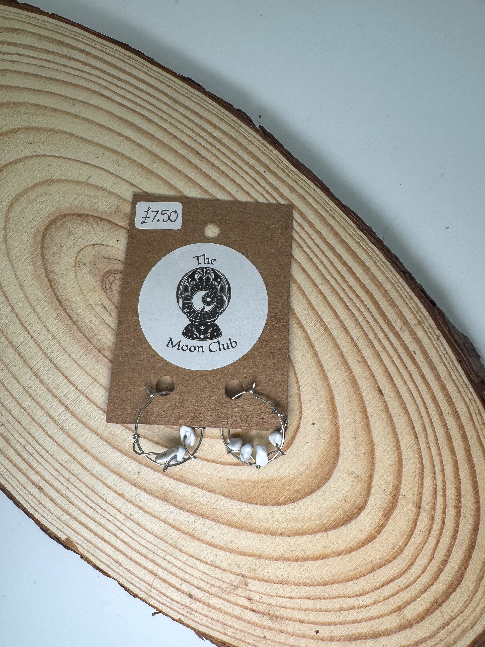 Pair of howlite earrings on a card with 'The Moon Club' logo, placed on a wooden surface.