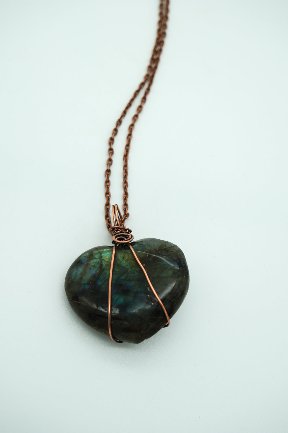 Heart-shaped stone pendant with copper wire wrapping on a white background