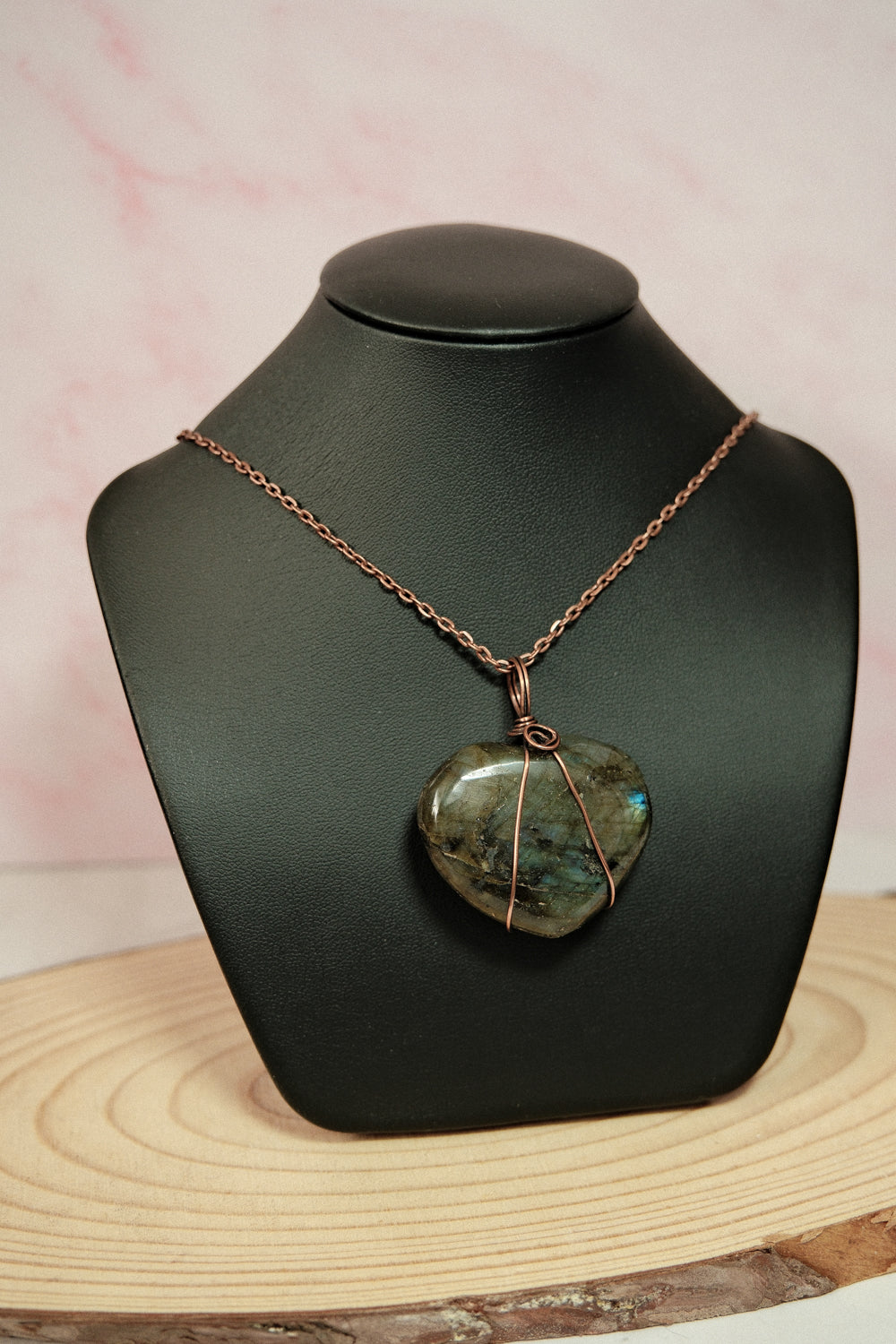 Necklace with a heart-shaped labradorite stone pendant on a black mannequin bust against a pink background.