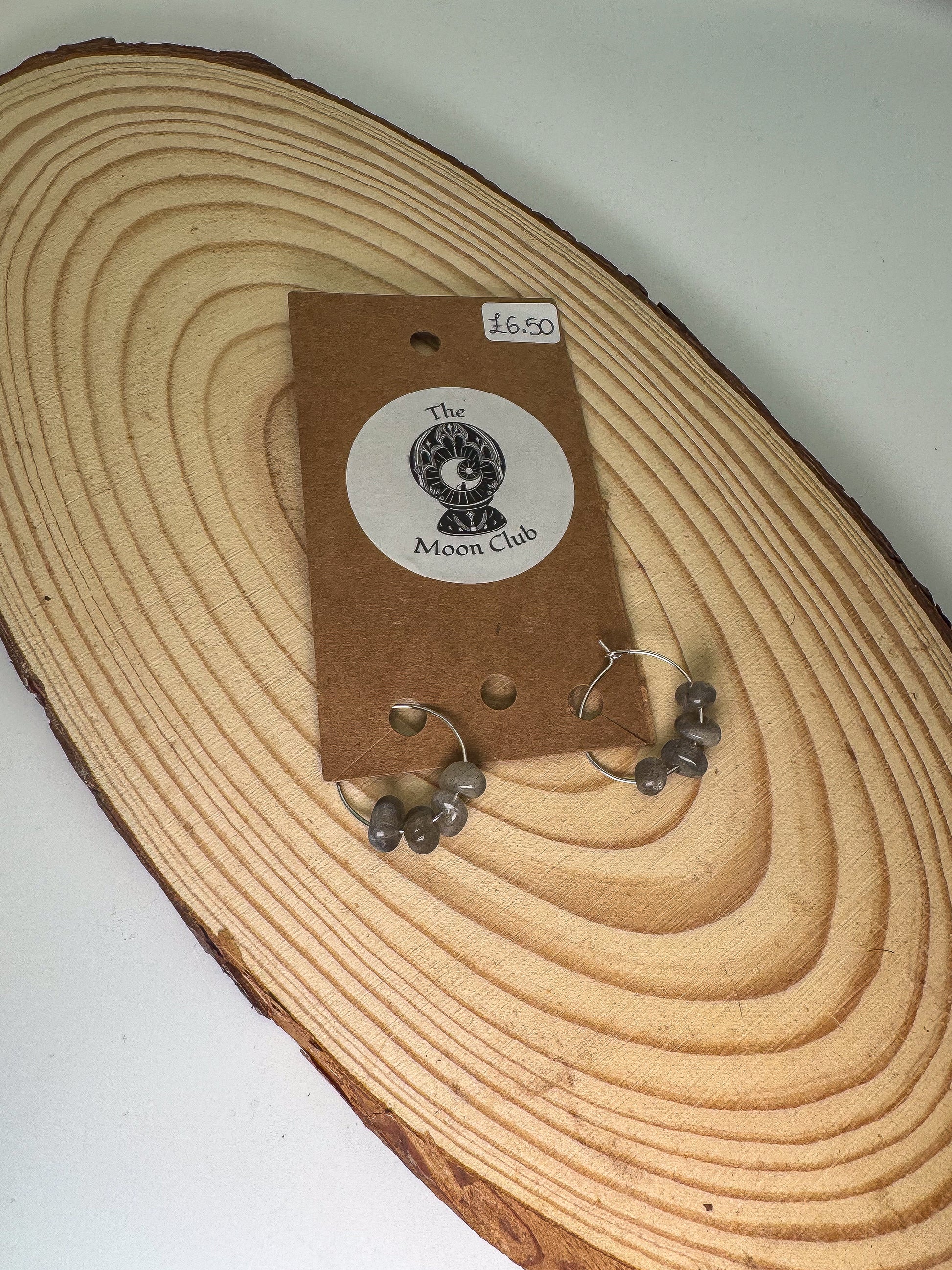 Pair of labradorite earrings on a wooden surface with a 'The Moon Club' label.