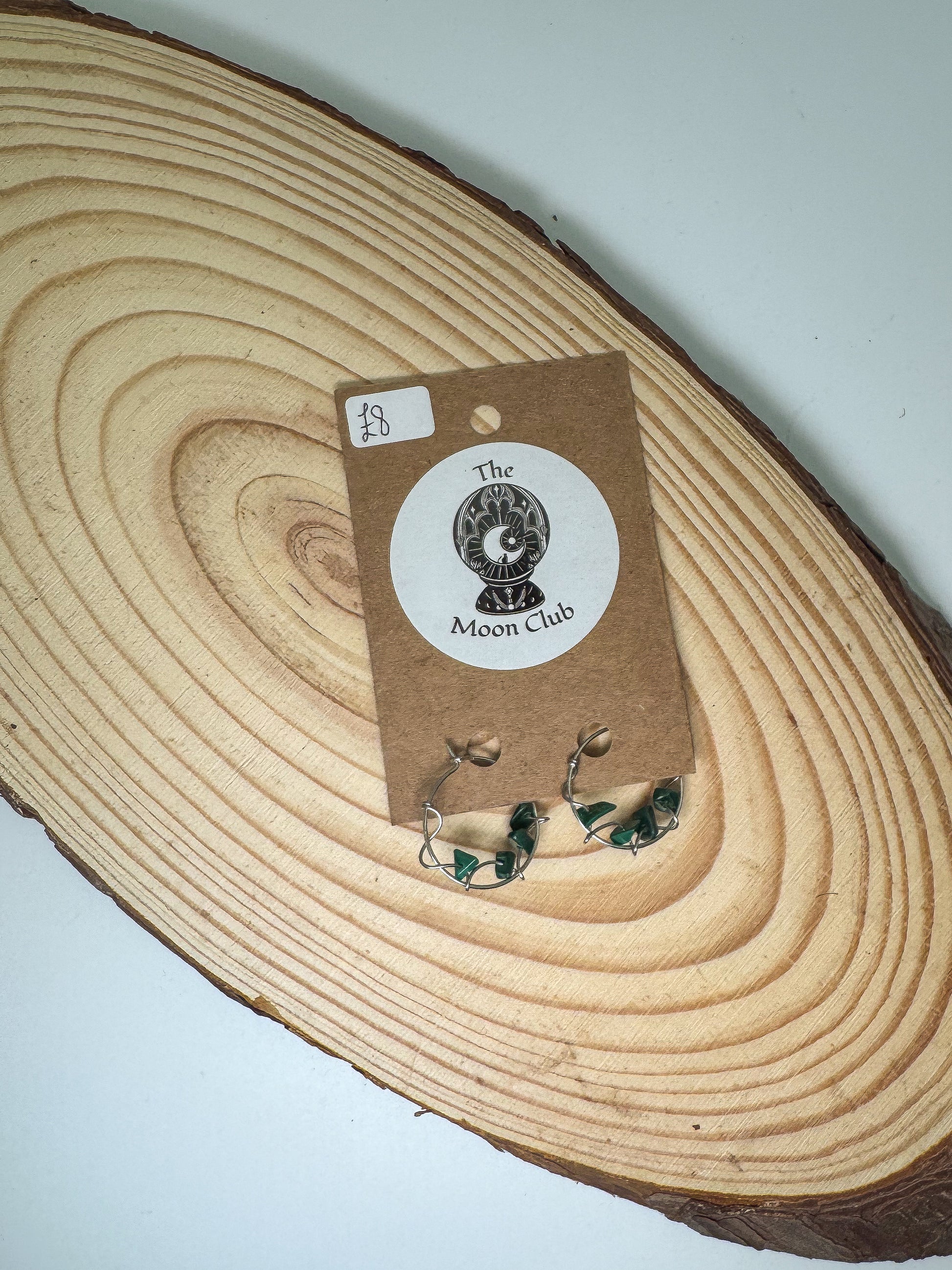 Pair of malachite earrings on a wooden surface with a 'The Moon Club' label.