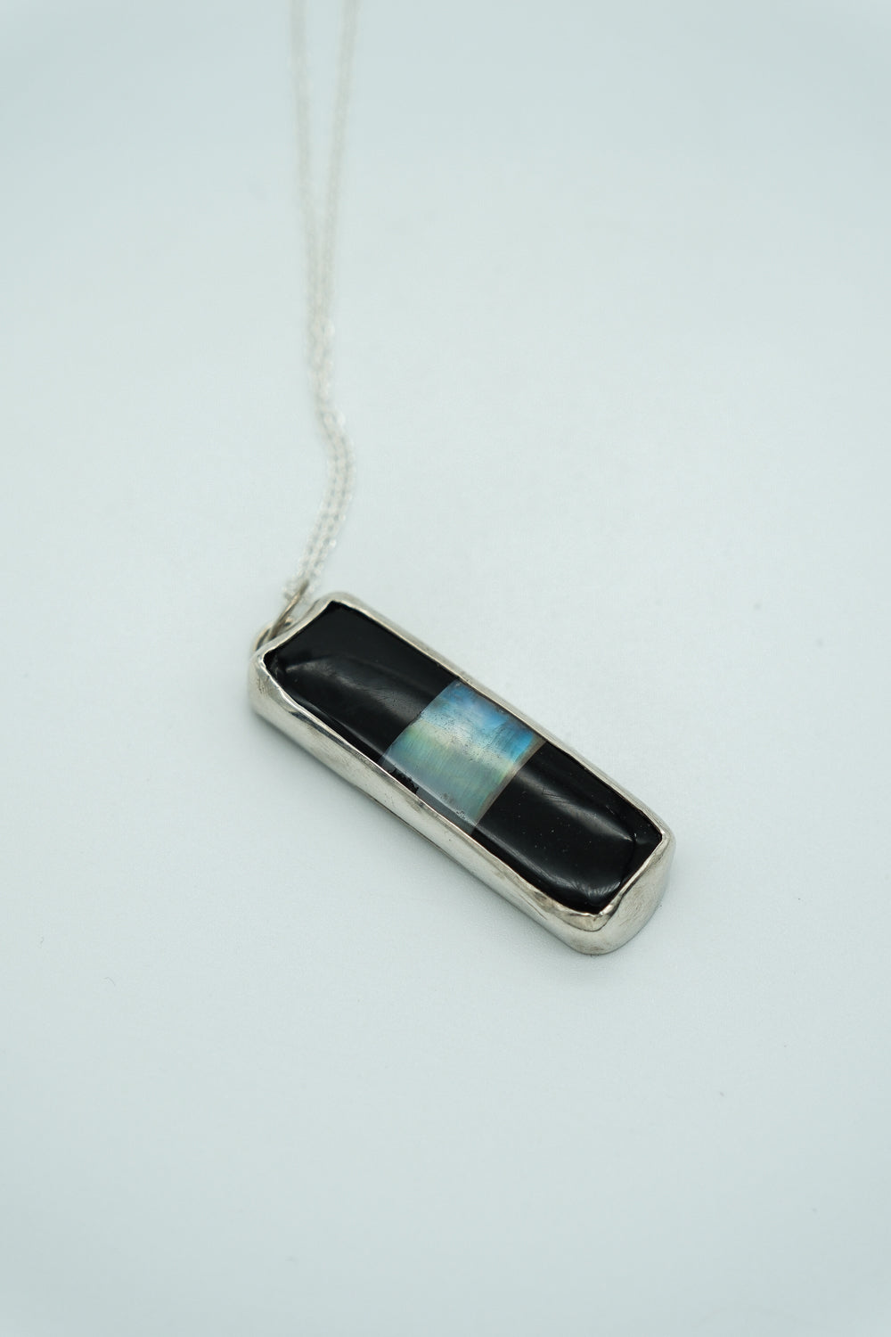 Necklace with a rectangular pendant featuring black and blue stripes on a light gray background