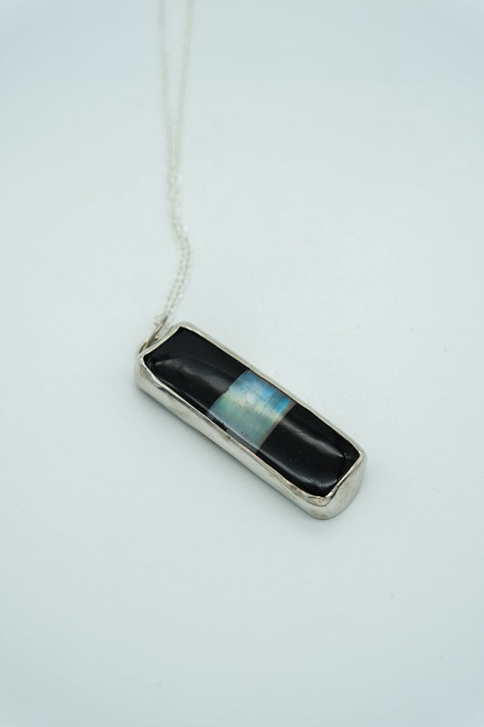 Necklace with a rectangular pendant featuring black and blue stripes on a light gray background