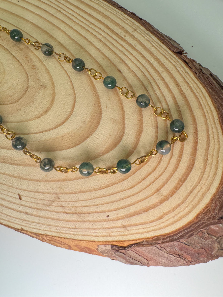 Necklace with green beads and gold chain on a wooden surface