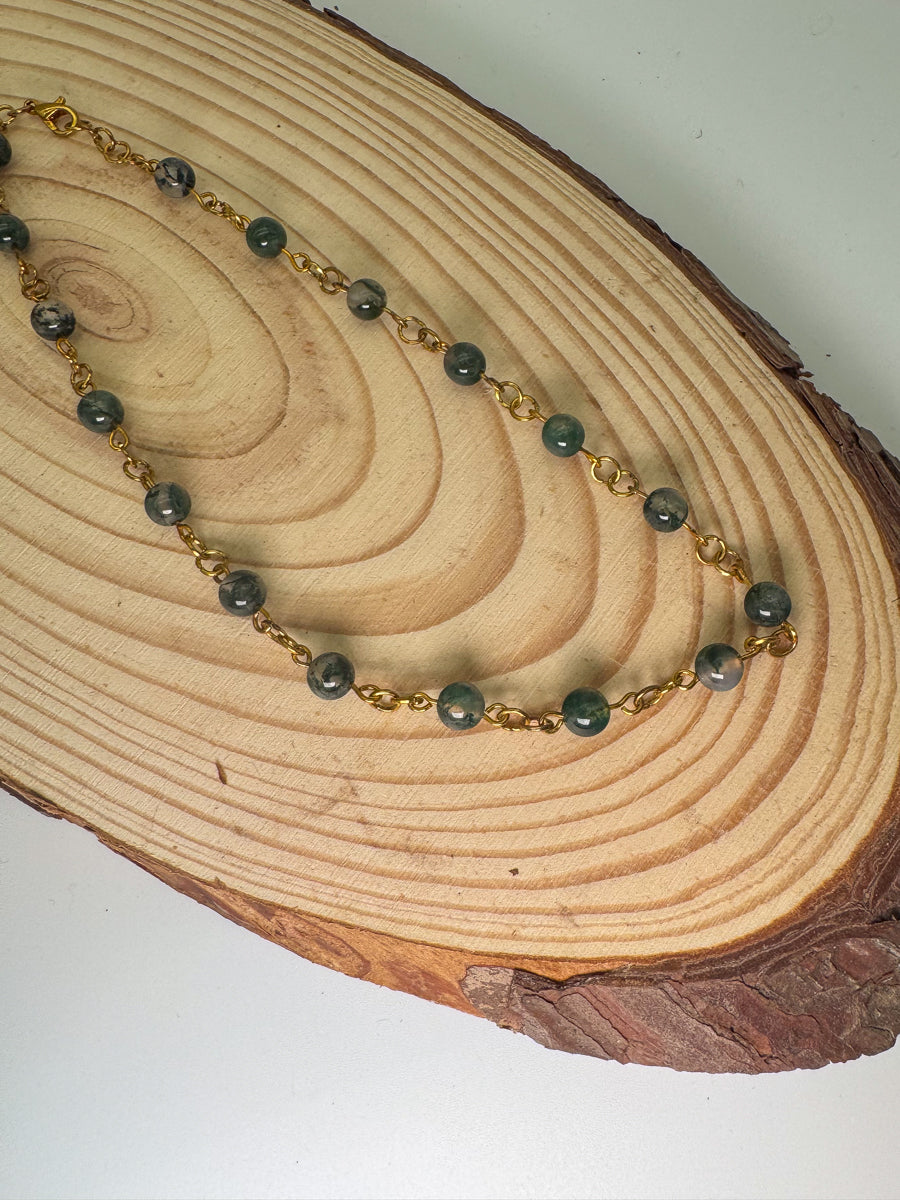 Necklace with green beads and gold chain on a wooden surface