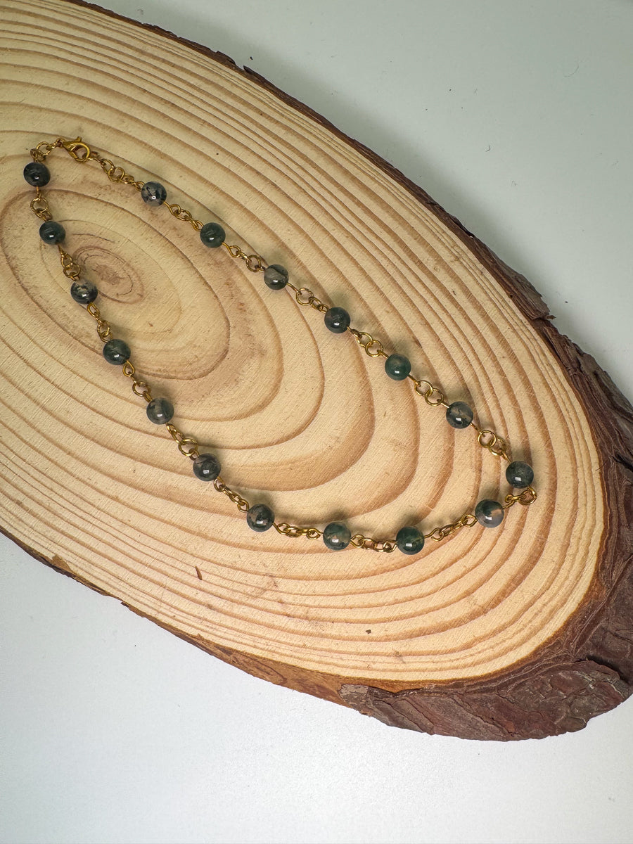 Necklace with green beads and gold chain on a wooden surface