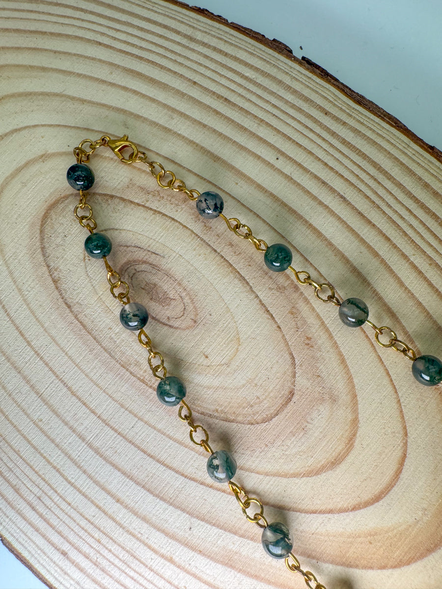 Gold chain necklace with green beads on a wooden surface