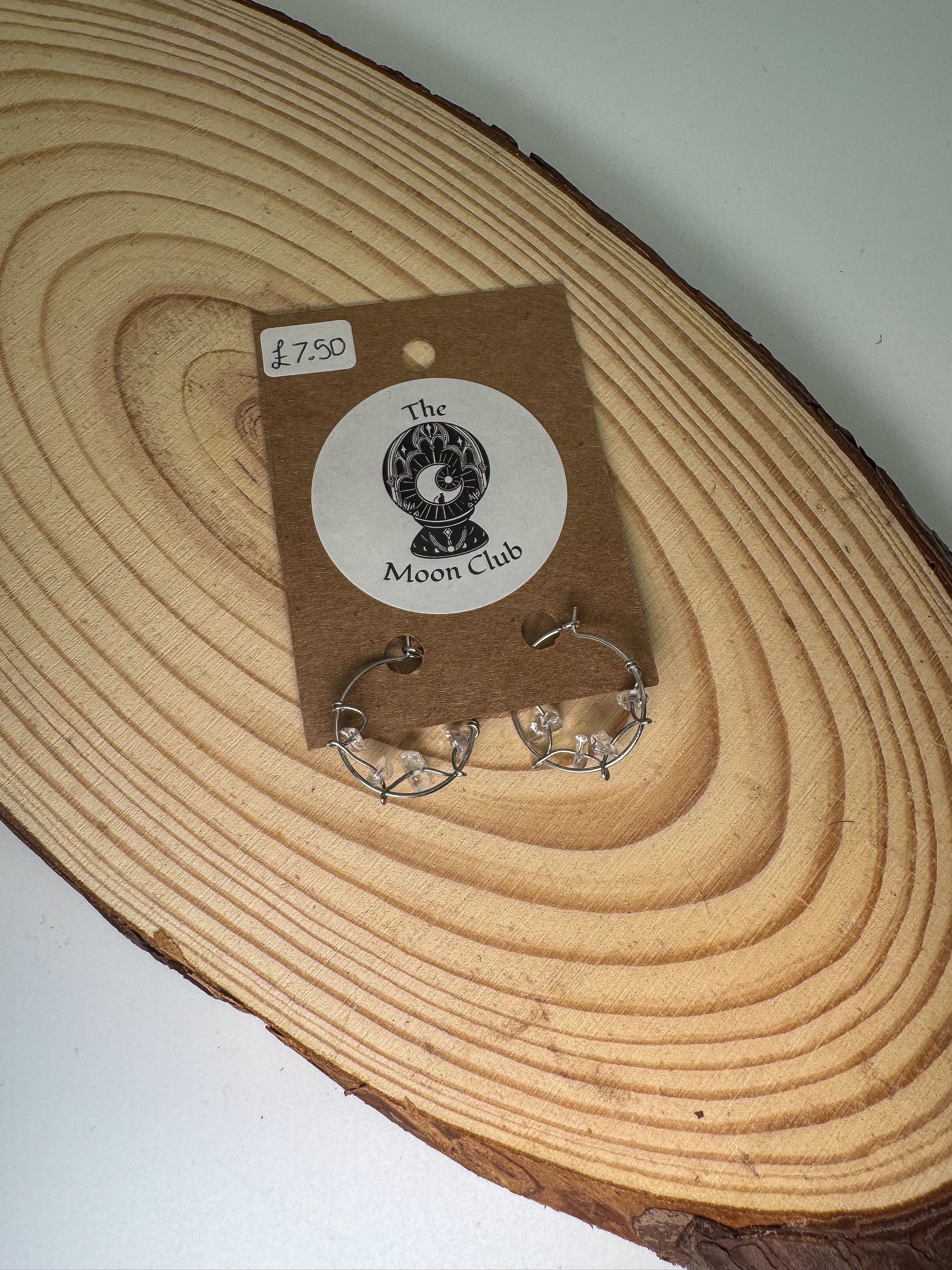 Quartz earrings on a 'The Moon Club' branded card over a wooden surface