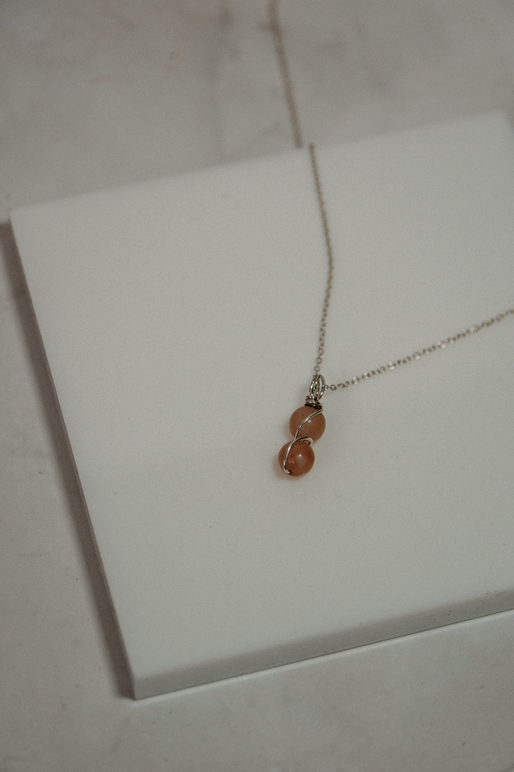 Necklace with two orange beads on a white card