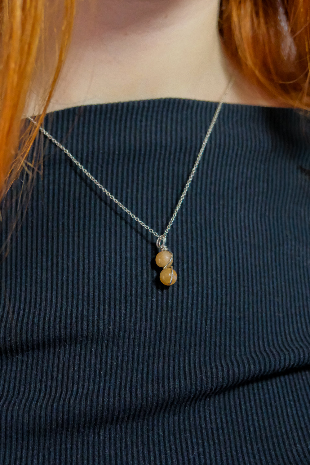 Necklace with two round beads worn by a person with red hair, against a black top.