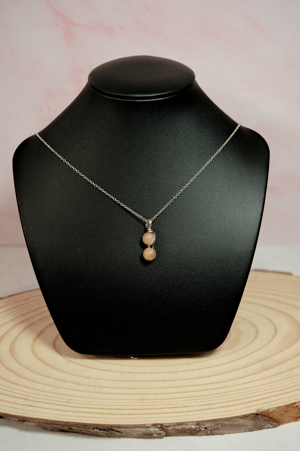 Necklace with a pendant on a black mannequin bust against a pink background