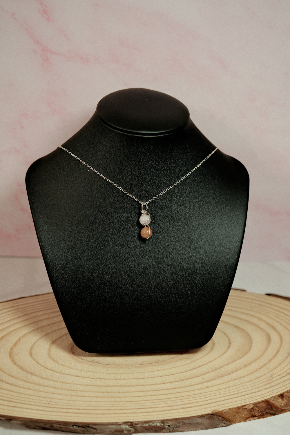Necklace with a pendant on a black mannequin bust against a pink marble background