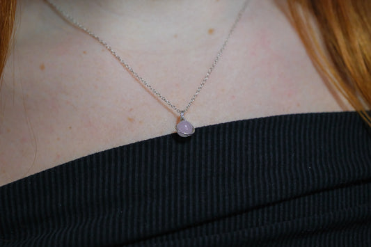 Necklace with a pink pendant worn by a person with red hair.