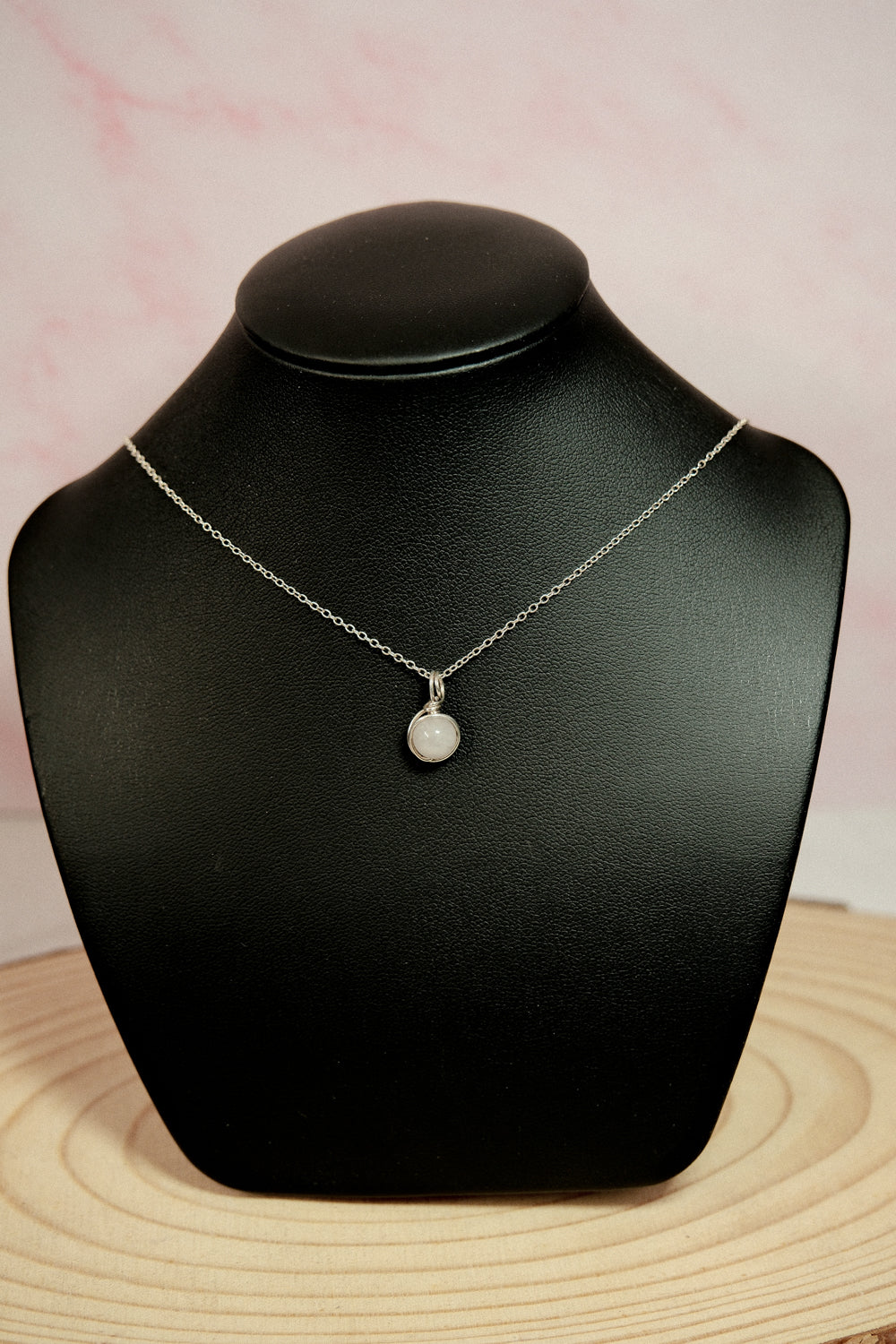 Silver necklace with a pendant on a black mannequin bust against a pink background