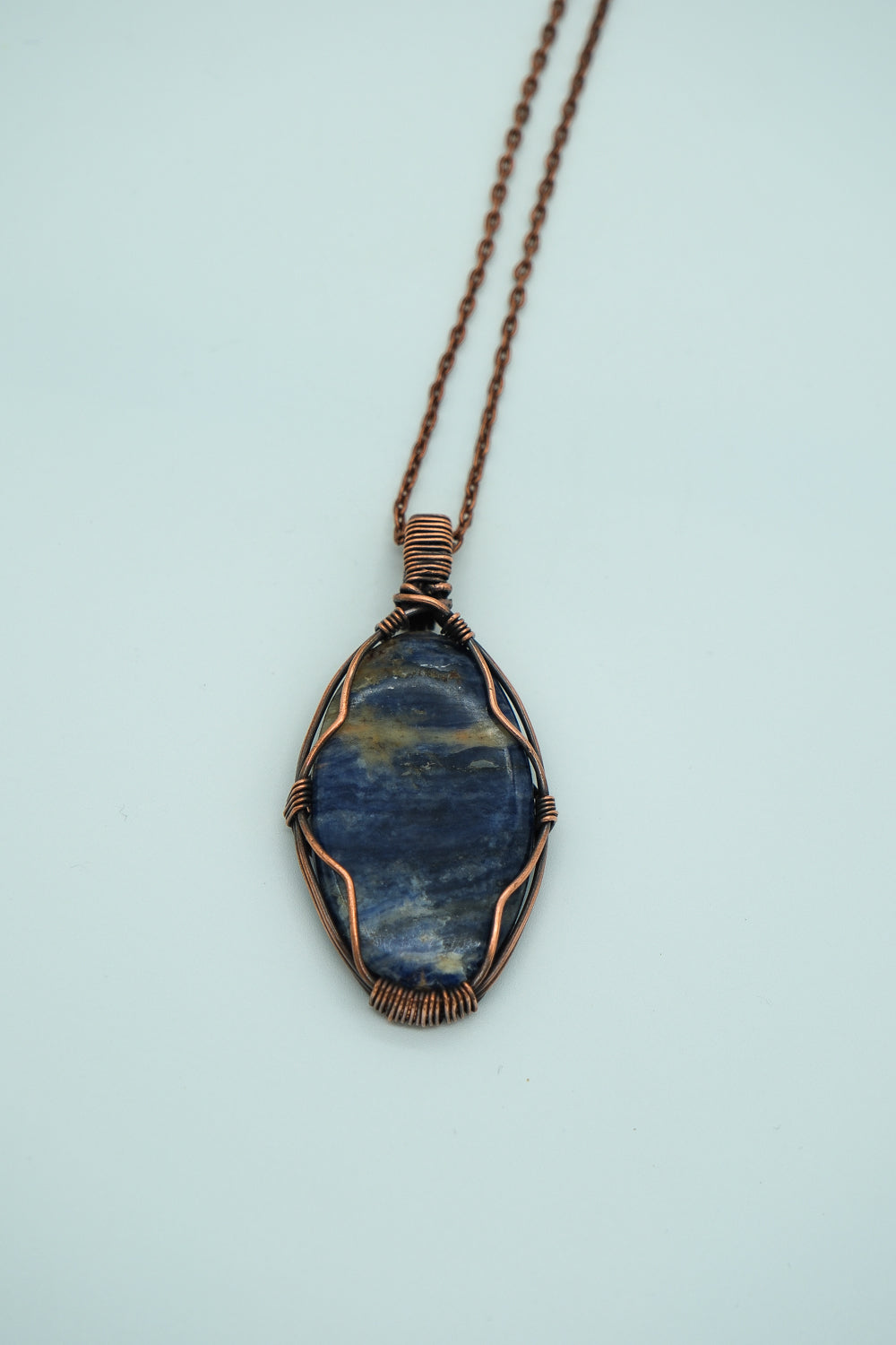 Blue stone pendant with copper wire wrapping on a light blue background