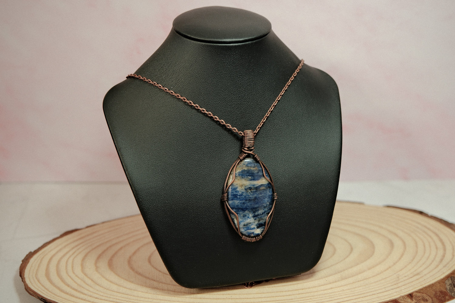 Necklace with a blue pendant on a black mannequin bust against a pink background