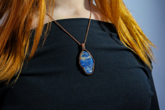 Person wearing a necklace with a blue pendant against a neutral background