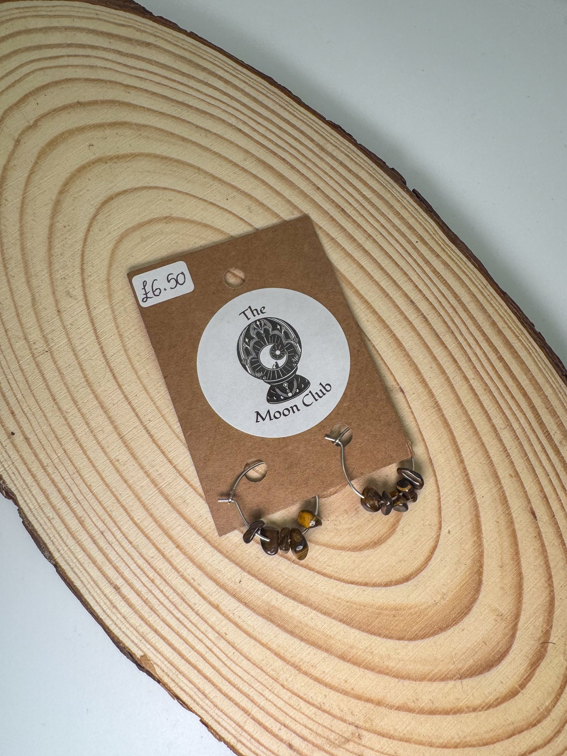 Pair of tigers eye earrings on a wooden display block with 'The Moon Club' label.