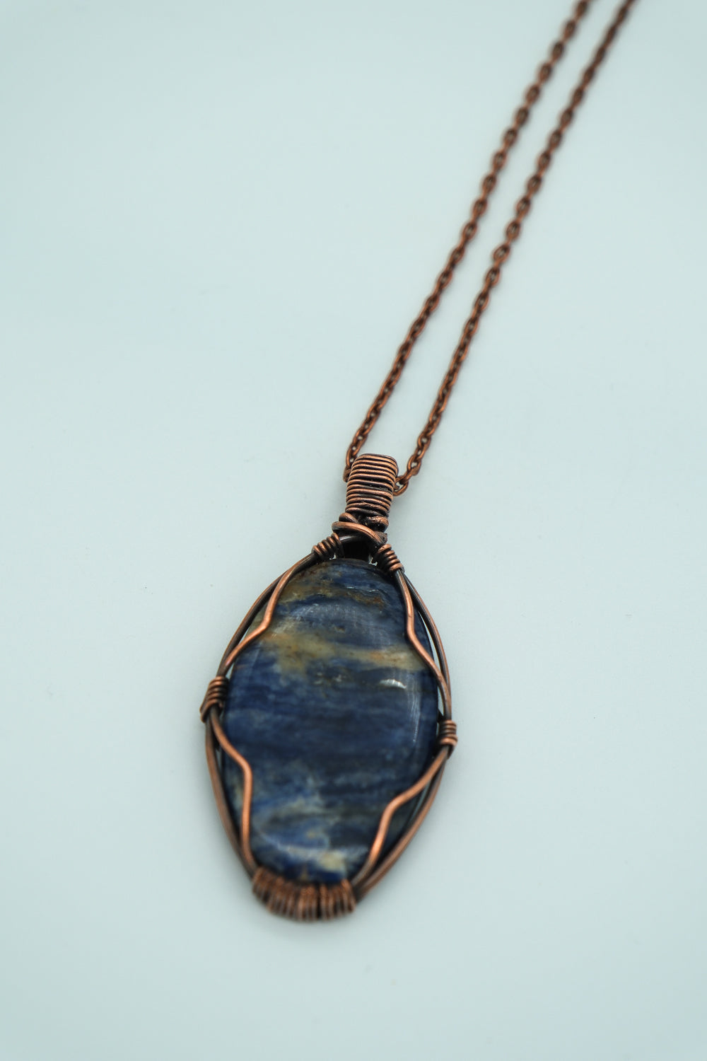 Blue stone pendant with copper wire wrapping on a light blue background